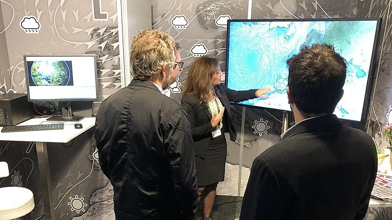 Visitors at the ask booth at IBC 2019 looking at a weather presentation on a large touch screen