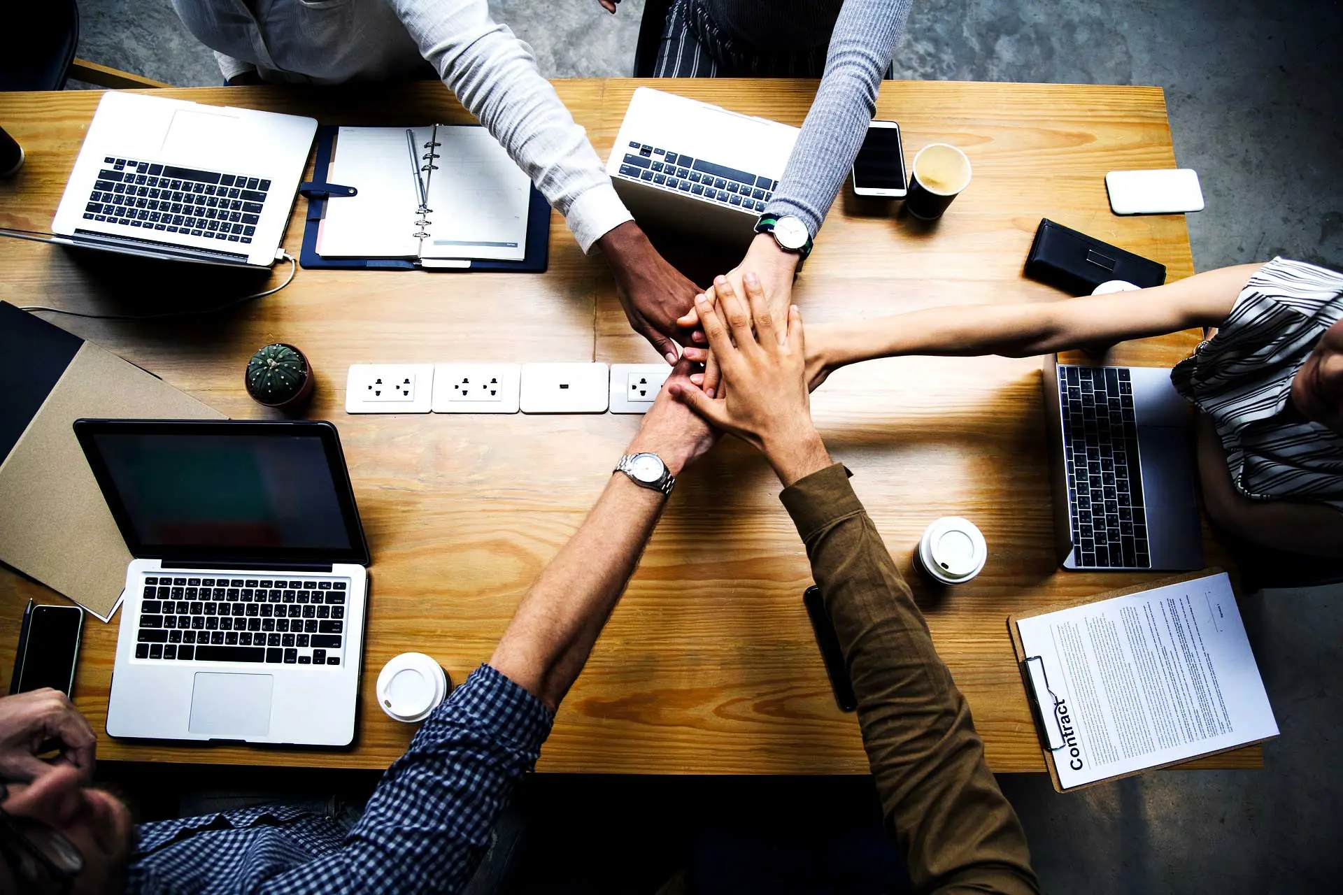 Team members joining hands above a table with laptops