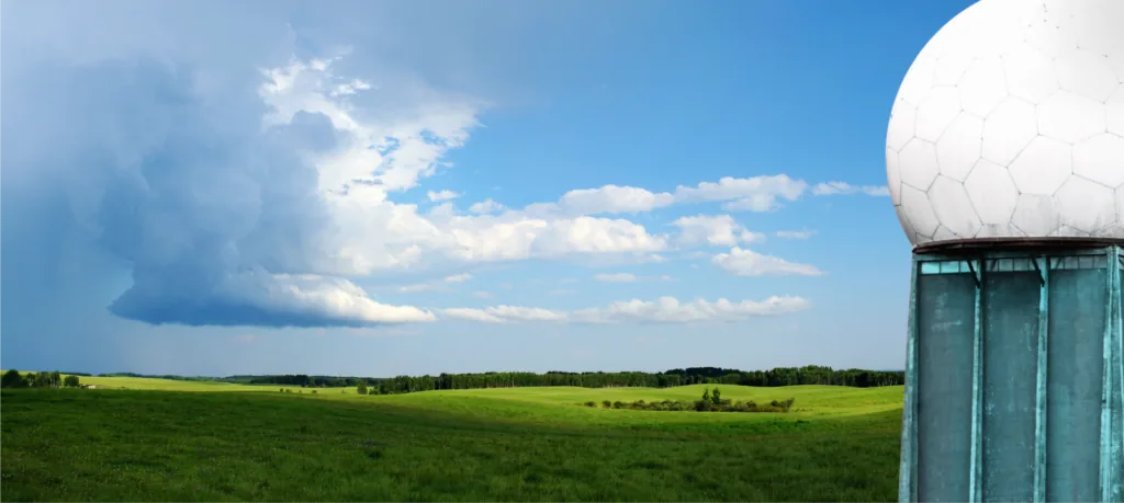 Weather radar dome next to a green meadow under a cloudy sky