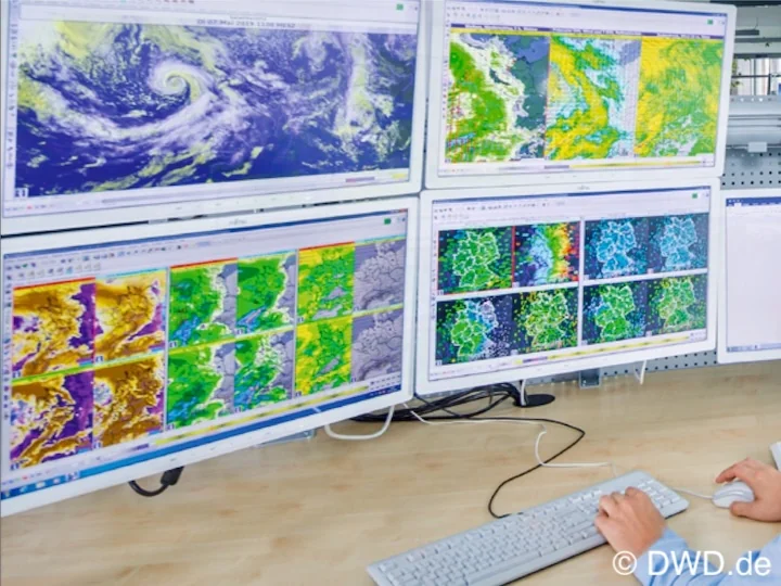 Forecaster working at a NinJo workstation with four monitors showing satellite images and weather model maps